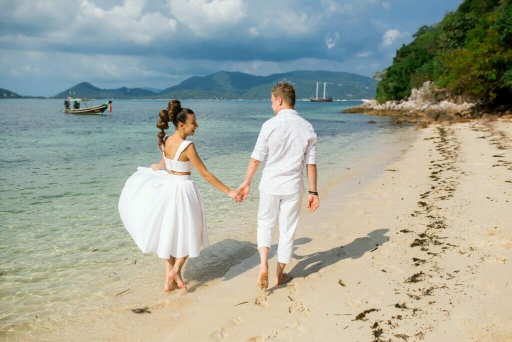 Male groom and female bride walking barefoot on beach